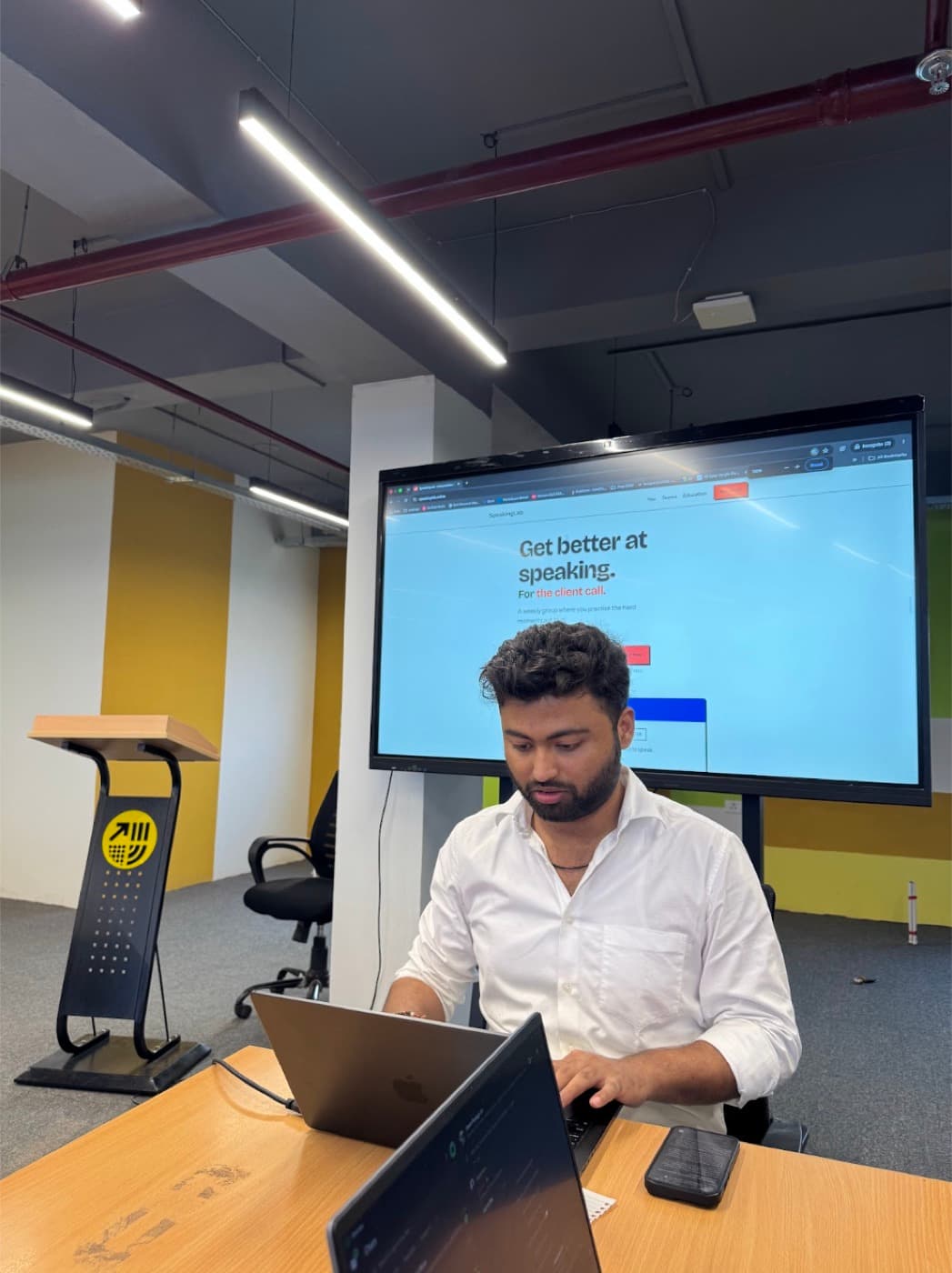 The host at a laptop in front of a screen showing SpeakingLab